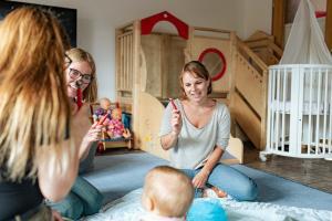 3 Pädagogische Fachkräfte sitzen mit Kleinkind im Kreis
