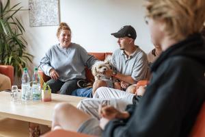 Pädagogische Fachkraft sitzt gemeinsam mit Jugendlichen und einem Hund auf Sofas einer Internatsgruppe