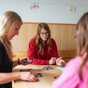 Pädagogische Fachkraft spielt mit 2 Jugendlichen ein Kartenspiel